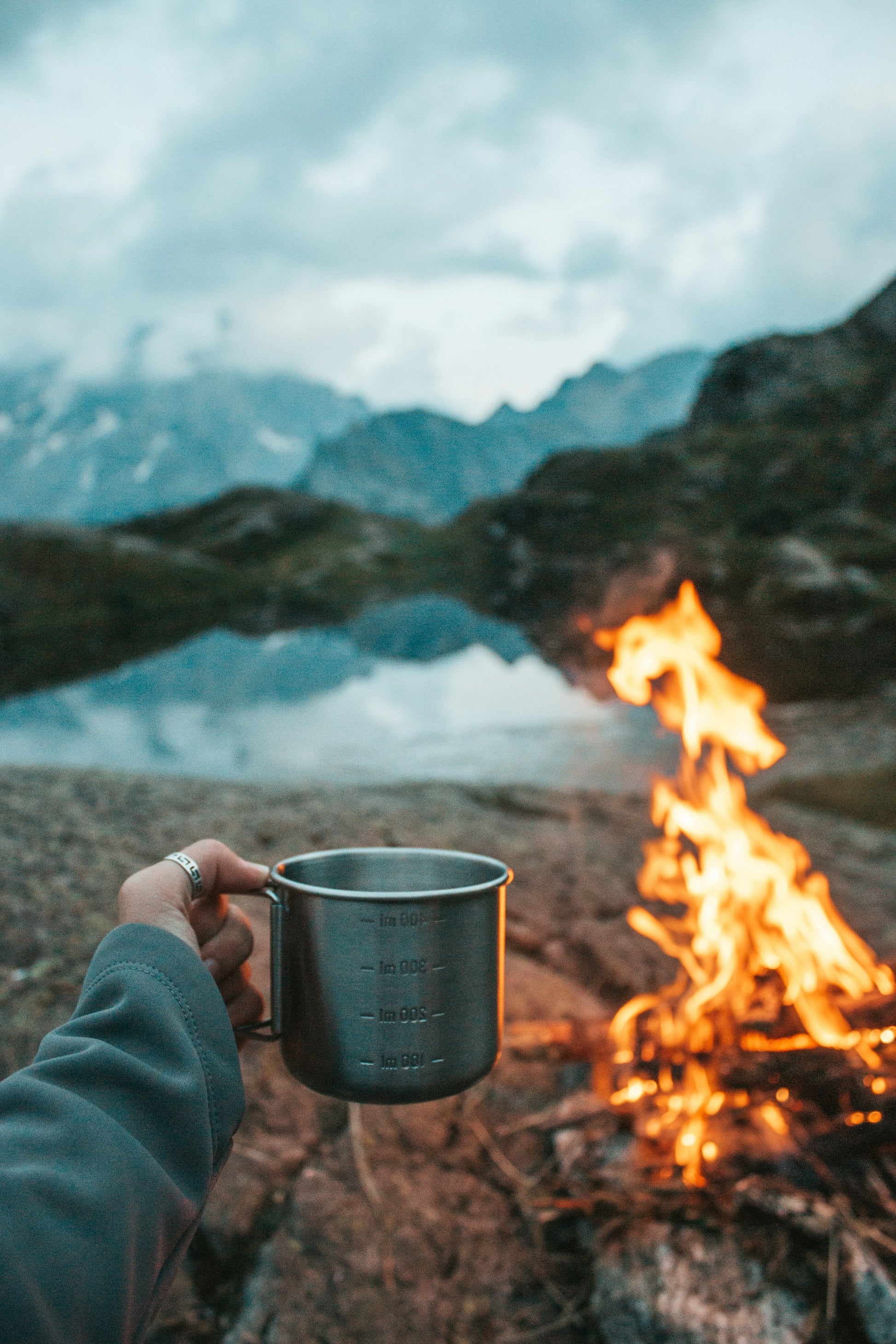 woman holding cup in front of fire and mountain scenery